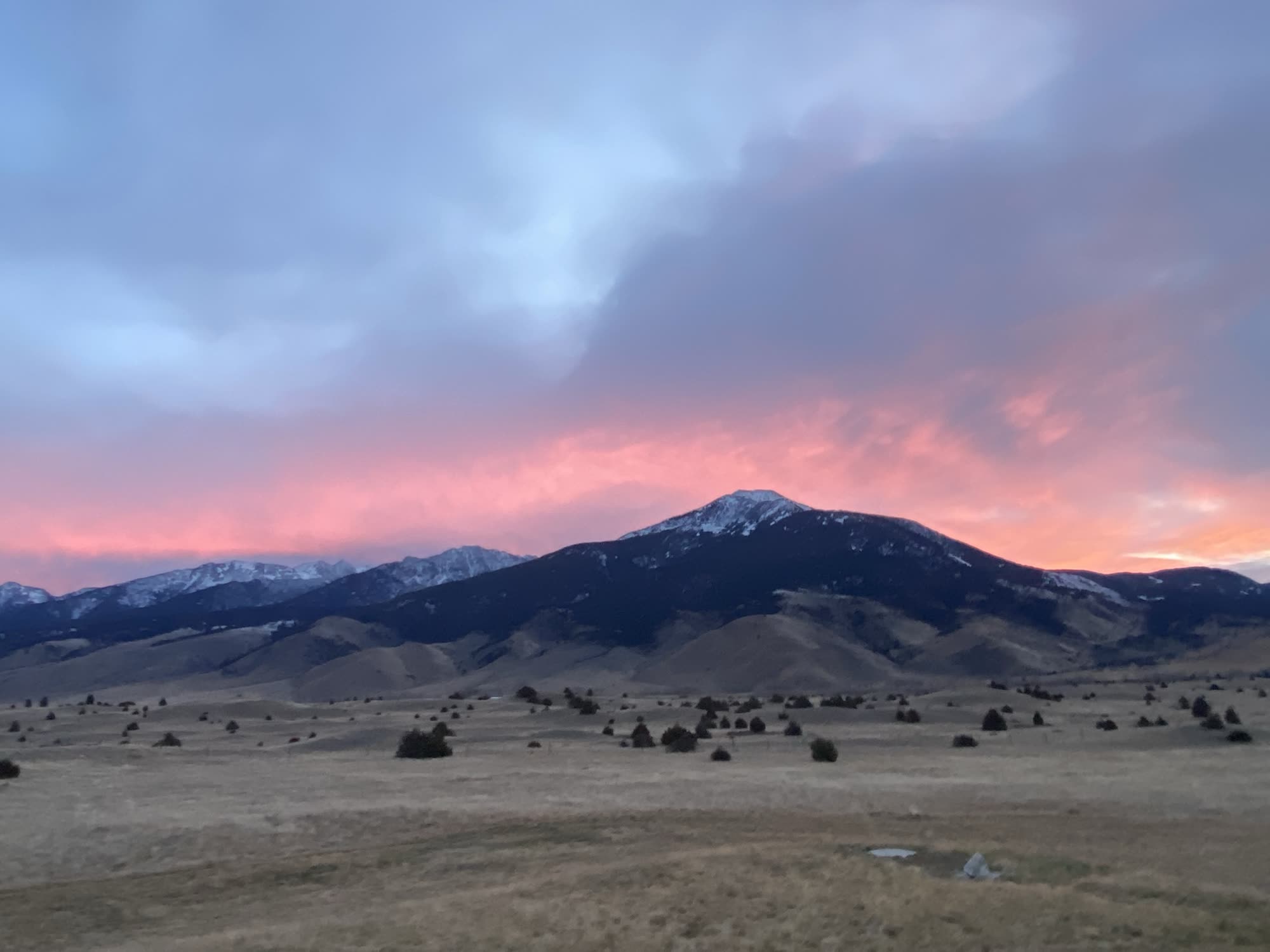 Pink sunset sky over a snow-dusted mountain and golden foothills